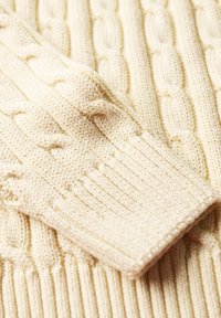 Pullover in maglia a treccia di colore avorio. Presenta motivi intrecciati in rilievo con polsini a coste. Tessuto morbido con orlo elasticizzato.