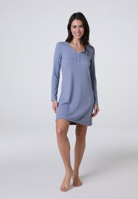 Vestito da notte azzurro chiaro con maniche lunghe, texture a costine, scollatura a V e patta con tre bottoni. Lunghezza sopra il ginocchio. Modello a piedi nudi.