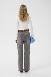 Grå jeans med vide ben, en brun skinnbelte og et blått tøystykke holdt i venstre hånd; brukt med en hvit genser med lange ermer.