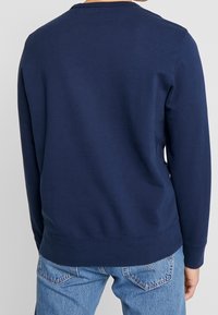 Marinblå sweatshirt med långa ärmar, rund halsringning, ribbade ärmslut och nederkant. Slät textur, avslappnad passform och inga synliga mönster eller detaljer.