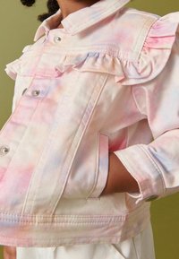 Veste en denim rose clair avec un motif tie-dye arc-en-ciel, détails froncés aux épaules, boutons-pression en argent et poches latérales.