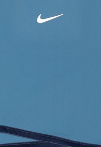 Šviesiai mėlynas sportinis marškinėlis, pagamintas iš lygaus audinio, su baltu Nike logotipu. Hemai yra tamsiai mėlyni akcentai.