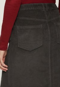 Jupe en velours côtelé gris avec des rainures verticales, dotée de deux poches arrière et d'une taille ceinturée. Accompagnée d'un haut à manches longues couleur rouille.