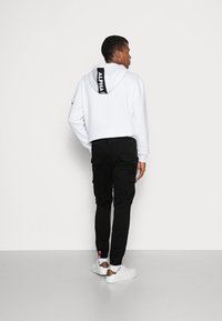 Sudadera blanca con el logo negro "ALPHA" en la parte de atrás, combinada con pantalones cargo negros y zapatillas blancas con un acento marrón.