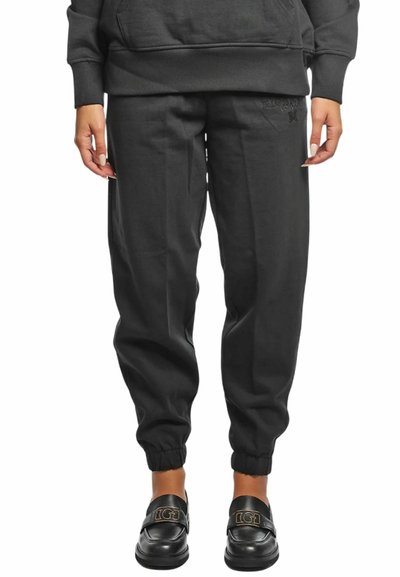 Persona che indossa pantaloni jogger neri con polsini elastici, una felpa nera abbinata e mocassini in pelle nera con un emblema dorato.