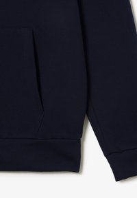 Felpa blu navy con tasca a canguro, polsini a coste e una texture liscia. Cuciture visibili lungo i bordi.