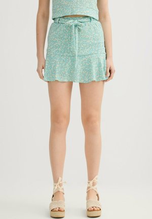 Mujer que lleva una minifalda floral azul claro con cintura ajustable y top a juego, combinada con sandalias de plataforma beige tejidas con cintas en el tobillo.