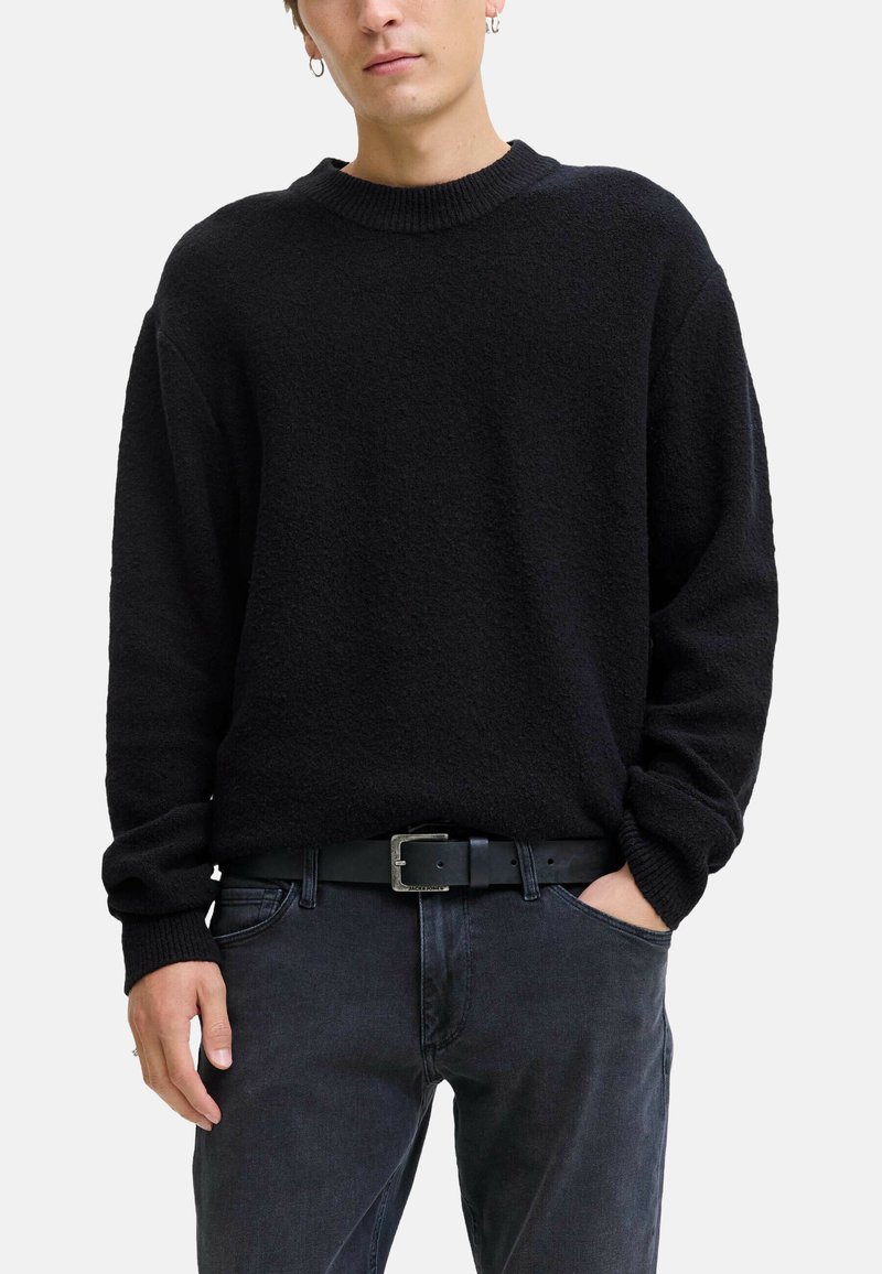 Maglione nero con trama e scollo girocollo a coste, abbinato a jeans scuri e cintura nera con fibbia rettangolare argentata.