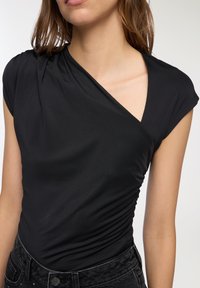 Top nero aderente con design drappeggiato, scollatura a V e maniche corte. Realizzato in un tessuto liscio con una texture sottile e dettagli arricciati.