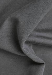 Mörkgrått stickat tyg med synlig struktur och mjuka veck som skapar en böjd, flödande form.