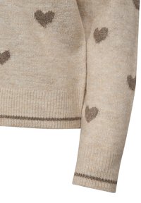 Beige tröja med bruna hjärtmönster, ribbade ärmslut och en horisontell rand vid fållen. Tillverkad av mjukt, texturerat material.