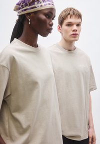 Tricouri bej din bumbac, cu mâneci scurte, decolteu rotund și un logo discret al brandului în față. Design simplu, cu croială lejeră.