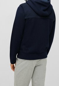 Mörk marinblå hoodie med en texturerad övre del och släta accenter samt ribbad nederkant. Kombineras med ljusgrå byxor.