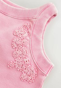 Pink striped sleeveless top with a textured crochet floral design on the left side. The fabric appears soft and slightly ribbed.