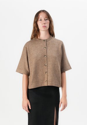 Kortermet, brun strikket cardigan med rund hals og syv store knapper foran, parret med et svart skjørt med slitt.