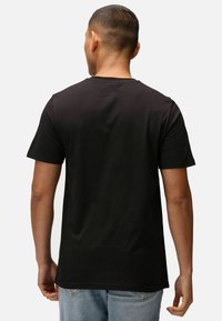 Černé bavlněné tričko s krátkým rukávem, kulatým výstřihem a volným střihem, spárované se světle modrými džíny. Jednoduchý design, bez viditelných vzorů.