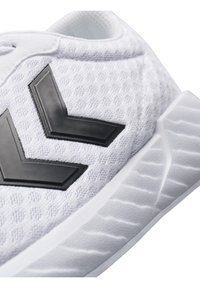 Białe buty sportowe z teksturowaną siateczką, czarnymi kątowymi akcentami oraz gumową podeszwą z wzorzystym bieżnikiem zapewniającym przyczepność.