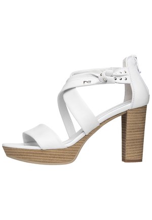 Białe sandały na obcasie z otwartym palcem, z krzyżującymi się paskami, blokowym obcasem o drewnopodobnej teksturze oraz akcentami w kolorze srebrnym.