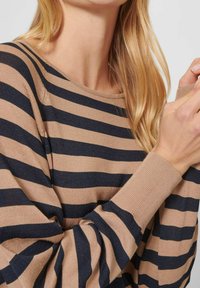 Beiger und marineblauer gestreifter Langarmpullover mit weitem Ausschnitt und gerippten Bündchen, der eine weiche Stricktextur aufweist.