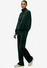 Donkergroene fluwelen trainingspak met hoge kraag, voorzak en geborduurd logo. Losvallende broek met zijzakken.