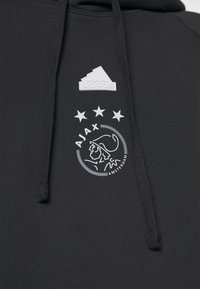Felpa nera con cappuccio e logo bianco Adidas sopra l'emblema del club calcistico Ajax Amsterdam, con tre stelle e il profilo di un guerriero.
