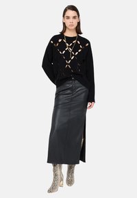 Maglione nero in maglia con motivi traforati, abbinato a una lunga gonna in pelle nera con spacco laterale e stivali con tacco stampa serpente.