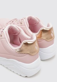 Jasnoróżowe buty sportowe z gładką syntetyczną cholewką, złotymi akcentami na pięcie i białą fakturowaną podeszwą. Perforowane części zapewniające wentylację.