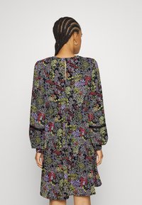 Vestido floral com um fundo escuro e padrões de flores coloridas. Mangas longas, corte descontraído e detalhe em forma de olho-chave nas costas.