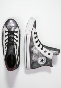 Vysoké tenisky s černým a stříbrným třpytivým designem, bílou gumovou špičkou, černými tkaničkami a kruhovou nášivkou loga na boku.