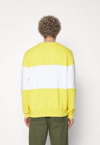 Gul och vit randig sweatshirt med långa ärmar och ribbade muddar. Mjukt tyg, avslappnad passform, med rundad hals och horisontella färgblock.