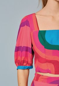 Farverig, mønstret bluse med korte puff ærmer. Har nuancer af pink, lilla, grøn og blå. Lavet af glat, letvægtsstof.