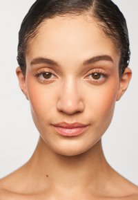 Close-up of a face with medium skin tone, smooth texture, light makeup, brown eyes, and wet hair, framed against a neutral background.