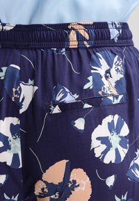 Květinové kalhoty s námořnickým podkladem. Obsahují elastický pas, nenápadnou kapsu a světle barevné květinové vzory v modrých a broskvových tónech.