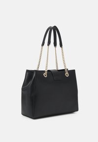 Sac tote en cuir noir avec des poignées en chaîne dorée brillante, forme structurée, texture lisse et fermeture à onglet à l'avant.