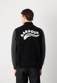 Sweater de malha com gola alta, corpo preto com mangas cinzentas e um logótipo "BARBOUR INTERNATIONAL" branco nas costas.