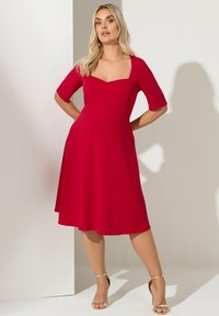 Czerwona dopasowana sukienka z krótkimi rękawami i kwadratowym dekoltem. Spódnica do kolan o rozkloszowanym kroju. Gładki materiał i minimalne akcenty.