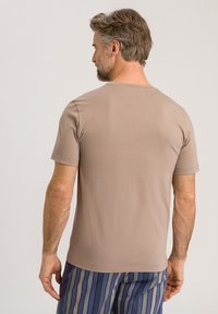 T-shirt di cotone beige con scollatura rotonda e maniche corte, caratterizzato da una texture liscia. Il modello indossa pantaloni corti a righe blu scuro e verde.