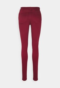 Jeans skinny burdeos con una textura suave, que presentan bolsillos traseros y una cinturilla de altura media. Ajuste entallado a lo largo de las piernas.