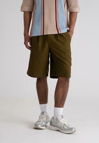 Olivegrønne shorts med en afslappet pasform og sidelommer, parret med en lysfarvet tekstureret striktrøje med lodrette striber.