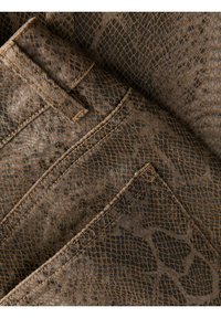 Rjavo tiskano tkanino z vzorcem kače s teksturirano površino, ki ima skrite žepe in kontrastno vezenje v mrežnem vzorcu.