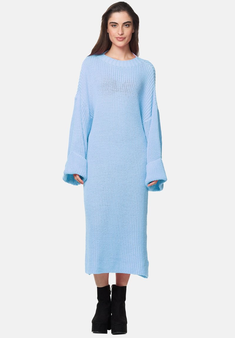 Abito maglione azzurro chiaro, maniche lunghe con ampi polsini, texture a costine, lunghezza al ginocchio, indossato con stivali neri con tacco.