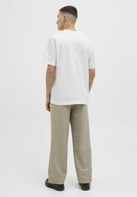 Hvid bomulds t-shirt med korte ærmer, rund halsudskæring og en afslappet pasform, parret med lyse beige brede bukser og mørke sko.