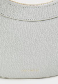 Gray leather handbag featuring a textured surface, gold hardware, and embossed branding along the bottom edge. Rounded top design.