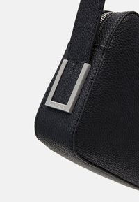Borsa a mano in pelle nera con superficie testurizzata, dotata di dettagli in metallo argentato e design triangolare elegante.