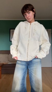 Un sweat à capuche zippé beige clair avec un cordon de serrage, des pochettes avant et des poignets côtelés, associé à un jean large bleu délavé.
