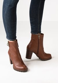 Bottines en cuir marron avec un détail de fermeture éclair, talons en bois et semelles texturées, portées avec un jean en denim foncé.
