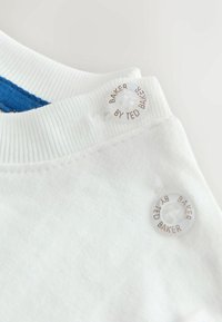 Biely bavlnený golier s modrým akcentom. Obsahuje priehľadný gombík s embosovaným nápisom "BAKER BY TED BAKER". Hladká textúra, jednoduchý dizajn.