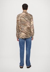 Majica z dolgimi rokavi iz gladkega blaga, z bež in črnim valovitim zebra potiskom, s kragnjo in gumbastimi manšetami. Nosite jo z modrimi kavbojkami.