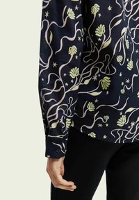 Navybluse med blomsterprint med lysegrønne og lavendelfarvede detaljer. Lange ærmer med knapmanchetter, letvægts stofstruktur.