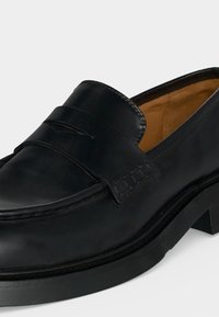 Mocassin penny en cuir noir avec un petit talon et des détails cousus, doublure intérieure couleur beige.